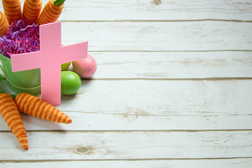 Pastel Christian Cross surrounded by Easter Decorations on white wood plank background