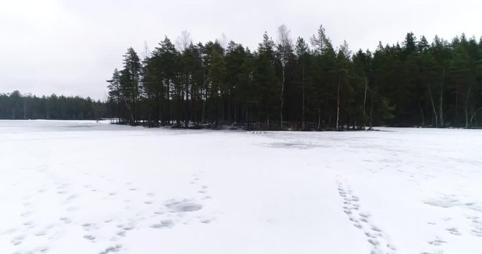 Cinema 4k aerial flying above snowy ice towards a marked ice hole or a glade, on a cloudy winter day, in Nuuksio national park, Finland