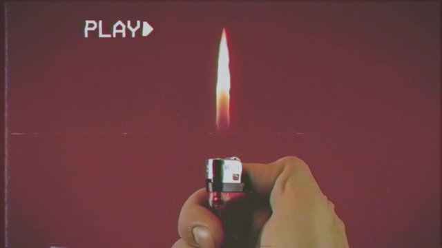 Fake VHS shot: operating a cigarette lighter; close-up on red background.
