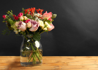 Glass vase with beautiful bouquet of  flowers on wooden table and black background