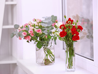 Beautiful roses in glass vases on windowsill
