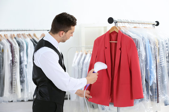 Man with steamer cleaning clothes in dry-cleaning salon