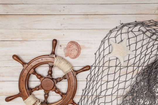 Rudder of sailing ship, fishing net with sea shells on wooden background