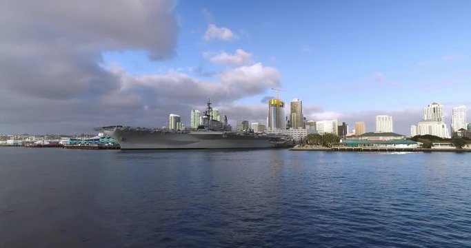 A wide, dramatic daytime establishing shot of the San Diego city skyline as seen from the bay.	The USS Midway aircraft carrier is in the foreground. Part 1 of 2.  	