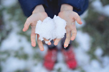 First snow on children's hands, red shoes in the background.