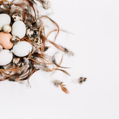 White, brown Easter eggs, quail eggs in nest decorated with feathers on white background. Flat lay, top view. Traditional spring concept.