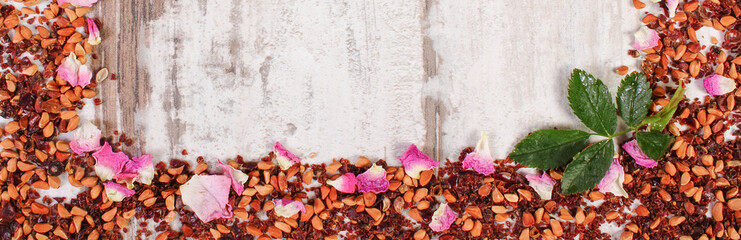 Frame of dried wild rose petals and tea grains on old board, copy space for text