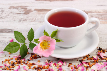 Cup of tea with wild rose flower on old rustic wooden background
