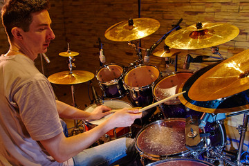 Fototapeta na wymiar Side View Of Young Drummer Playing Drum Kit In Studio