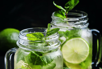 Iced green tea with lime and mint in glass jars, dark background, selective focus