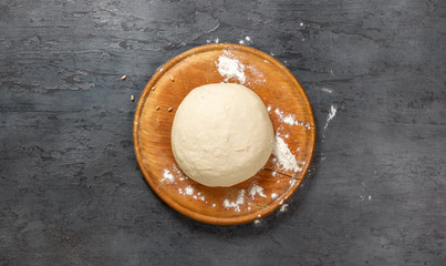 Fresh dough on wooden round board on dark background