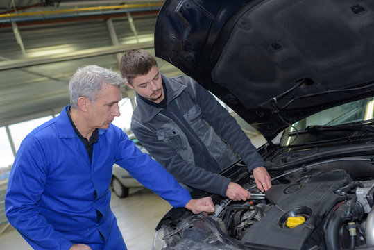 two professional car mechanics checking up engine