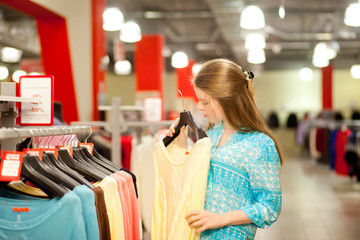 Young woman chooses clothes and looks in the boutique, shopping center or store, shopping