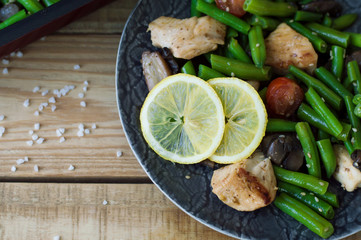 Plate with baked green beans, chicken breast, mushrooms, red cherry tomatoes, sesame seeds and lemon. Hot salad. Balanced and healthy meal