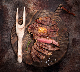 Sliced medium rare grilled beef steak ribeye on a brown rusty background