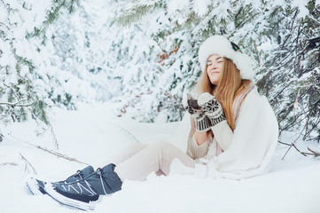 Beautiful woman is drinking tea on the background of a winter fairy-tale forest