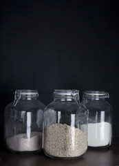 Three huge glass jars with oatmeal and flower on dark black background