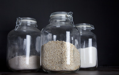 Three huge glass jars with oatmeal and flower on dark black background