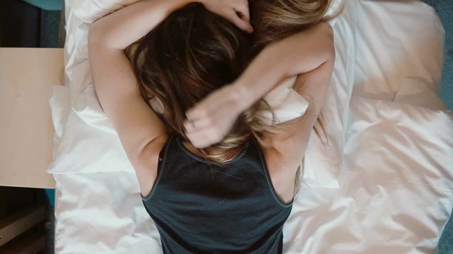 Tip view of angry woman falls face down on the bed in room. Sad girl beating her fist the pillows