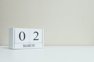 Closeup white wooden calendar with black 2 march word on blurred white wood desk and cream color wallpaper in room textured background with copy space , selective focus at the calendar