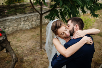 Fototapeta premium Groom kissing bride on neck background wooden stump with wedding bouquet.