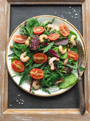 Homemade salad with arugula and tomatoes shrimp with capers on a white plate on a dark background in a wooden frame
