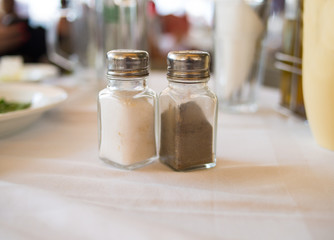 salt and pepper in a transparent glass containers on a table at lunchtime on a white tablecloth...