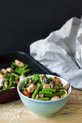 Vertical photo of hot salad in a blue bowl: green beans, chicken meat, cherry tomatoes, lemon, mushrooms and sesame seeds