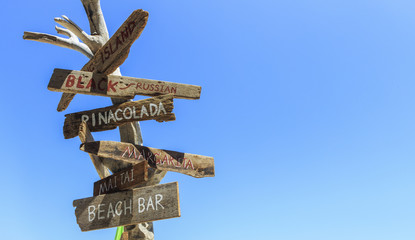 Old wooden sign on tropical beach with blue sky, over light