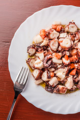 Octopus salad on plate with fork. Wood table in background.