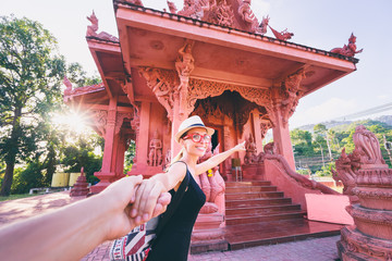 Obraz premium Follow me. Travel by Asia. Young woman holding boyfriend's hand showing temple on Samui Island in Thailand.