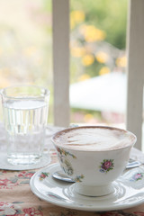 Cafe art latte coffee in the vintage cup on the tabel with a glass of water on the table