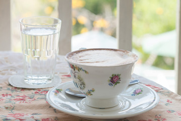 Cafe art latte coffee in the vintage cup on the tabel with a glass of water on the table