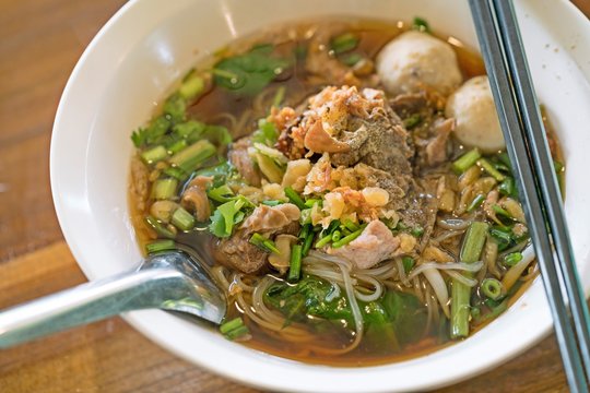 Thai food : Rice noodle soup with stewed pork and pork balls with soup on wooden table.
Thai Noodles style.