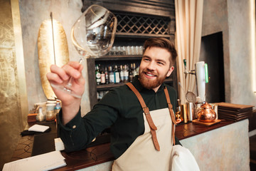 Attractive young bearded man bartender standing in cafe.