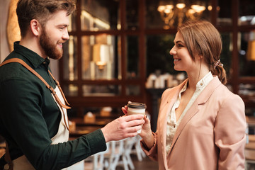 Attractive young man waiter standing in cafe gives the coffee