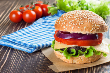 Homemade cheeseburger on brown wooden surface.
