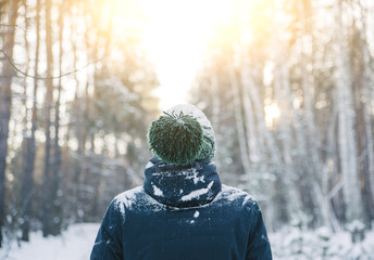 man covered in snow wearing a green beanie in the winter cold sunny forest