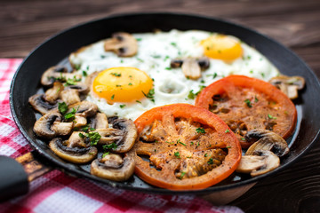 Fried eggs with mushrooms and tomato on dark wooden table