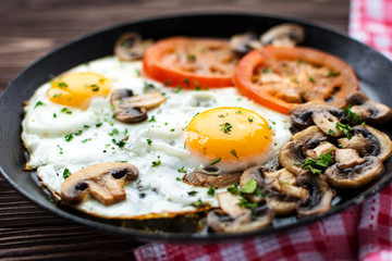 Fried eggs with mushrooms and tomato on dark wooden table