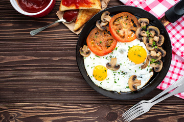 Fried eggs with mushrooms and tomato on dark wooden table