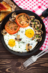Fried eggs with mushrooms and tomato on dark wooden table