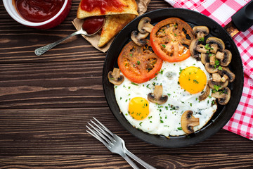 Fried eggs with mushrooms and tomato on dark wooden table
