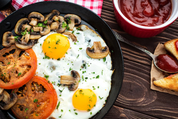 Fried eggs with mushrooms and tomato on dark wooden table