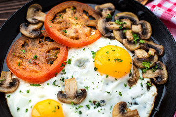 Fried eggs with mushrooms and tomato on dark wooden table
