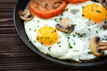 Fried eggs with mushrooms and tomato on dark wooden table