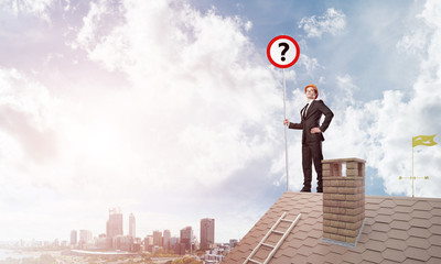 Businessman on brick house roof showing banner with question mark. Mixed media