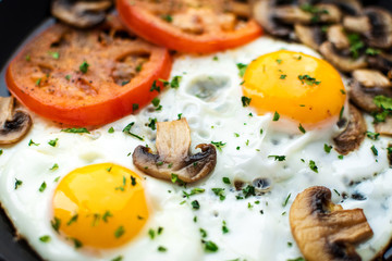 Fried eggs with mushrooms and tomato on dark wooden table