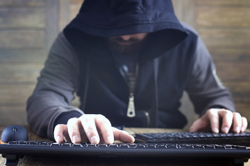 hacker in the black hood in a room with wooden walls