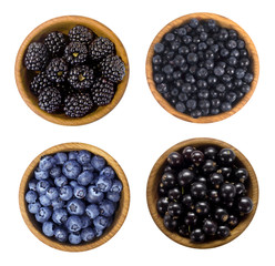 Black and blue berries. Blackberries, blueberries, currants and blueberries in a wooden bowl isolated on white background. Top view. Berries closeup.